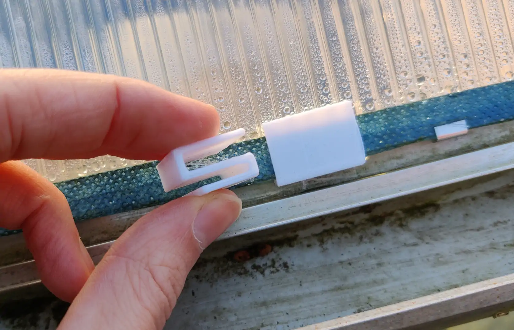 A white plastic clip, shaped as a square &ldquo;Z&rdquo;, showing a side profile next to one in use at the bottom of a roof pane