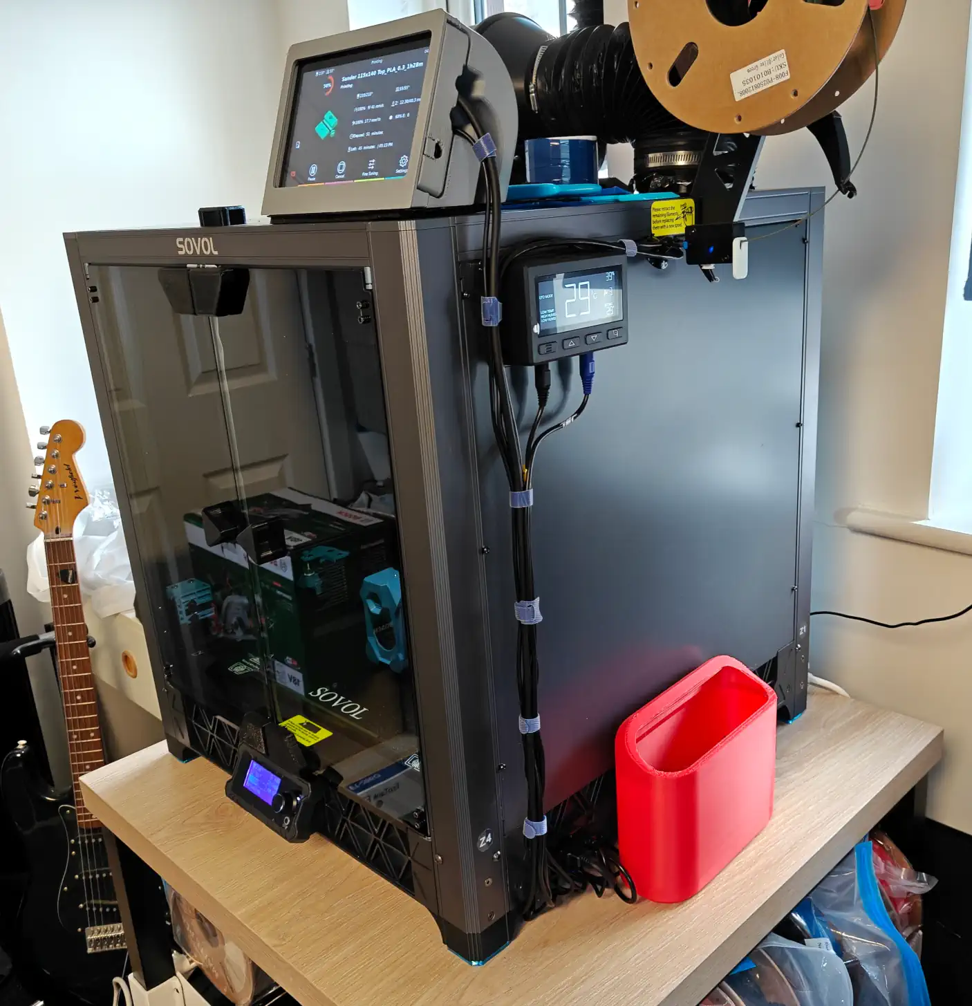 Side angled view of the printer, showing a control panel and cabling, along with a small bucket