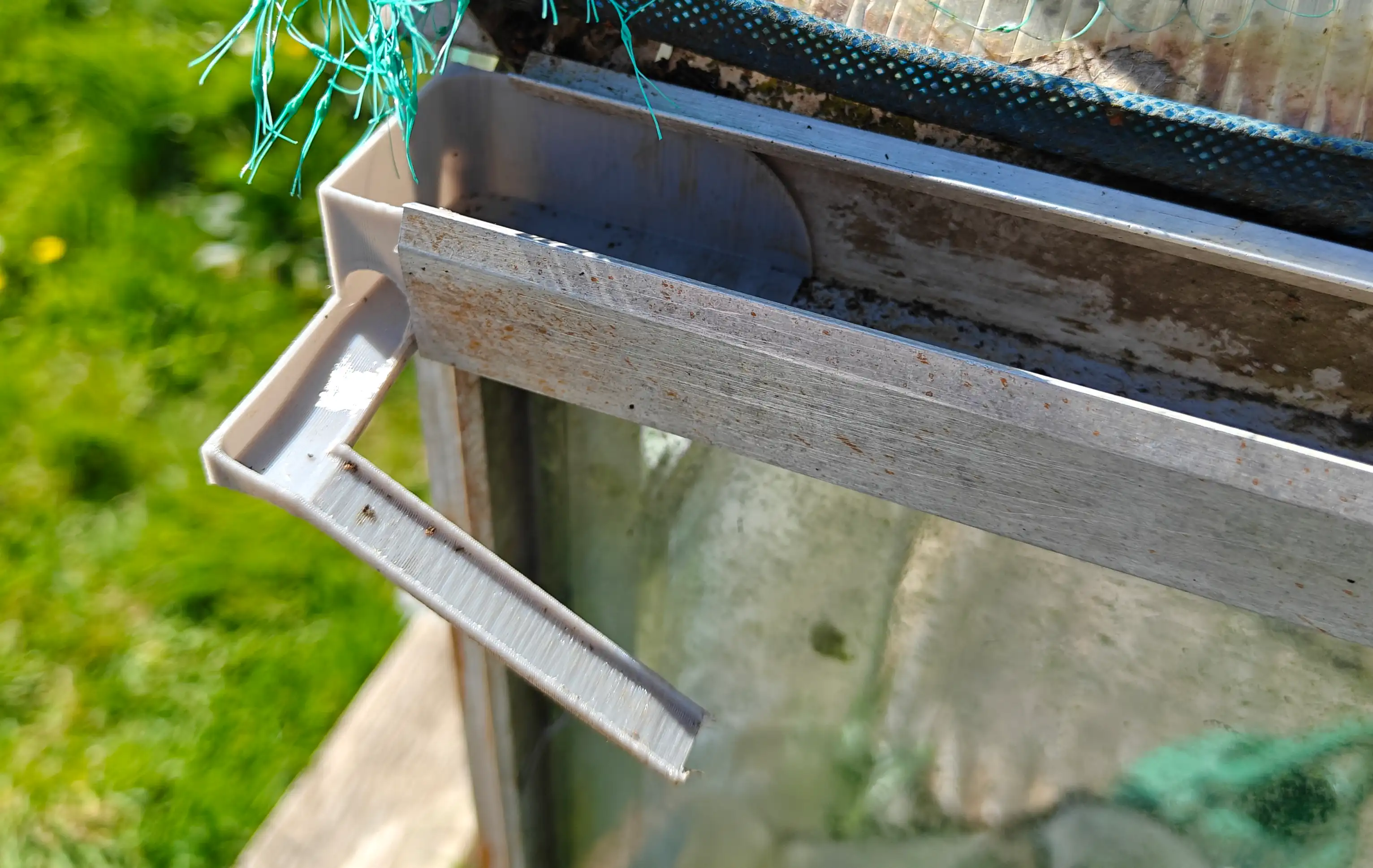 A close view of the edge of a greenhouse outer side channel, with a plastic part closing off the end, with a little hole in the edge and a &ldquo;slide&rdquo; of sorts then leading out and downward by an inch or two
