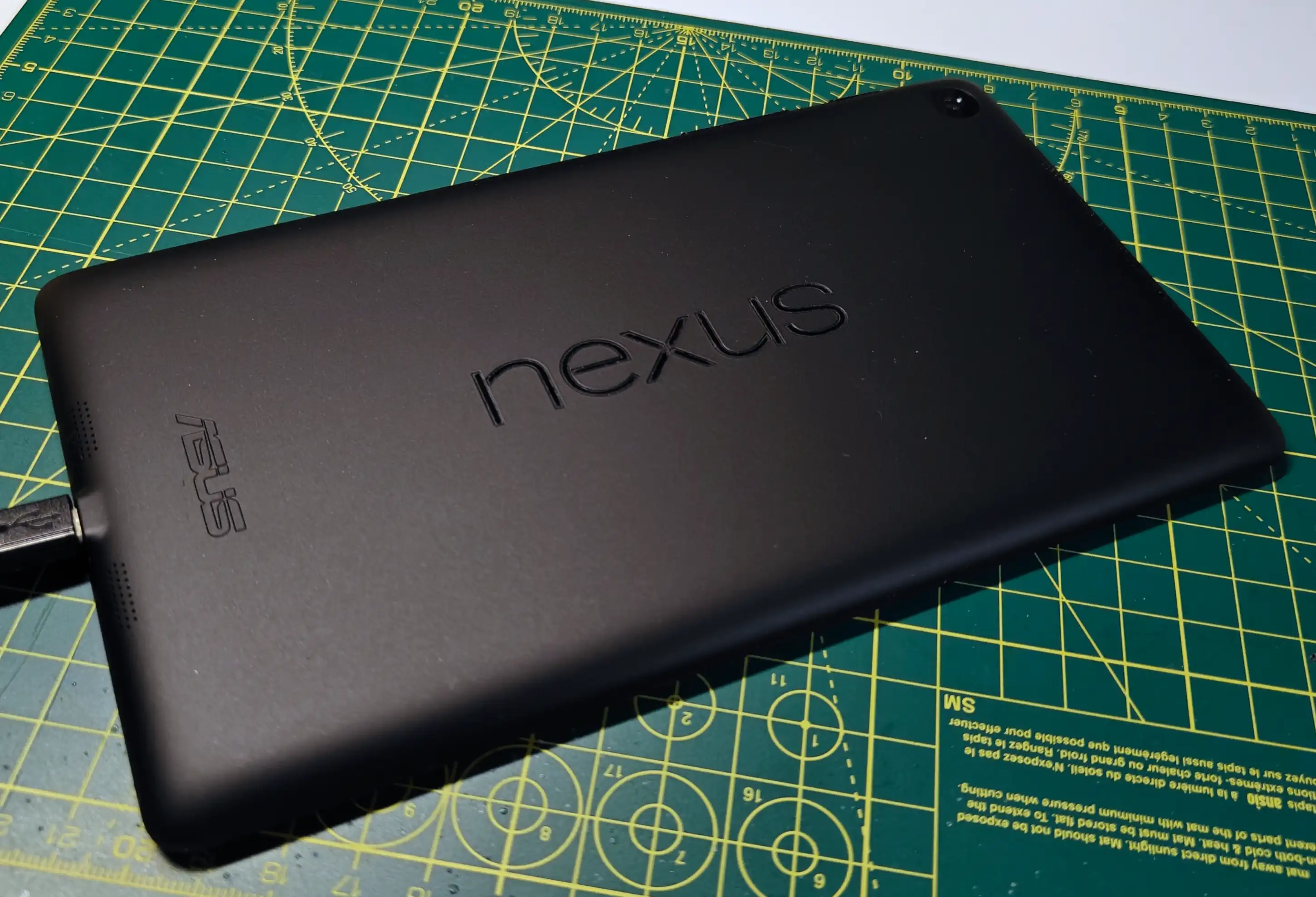 A Nexus 7 tablet, face down. The back appears matte black and slightly textured. The lower case word &ldquo;nexus&rdquo; is etched into the back, along with the Asus logo