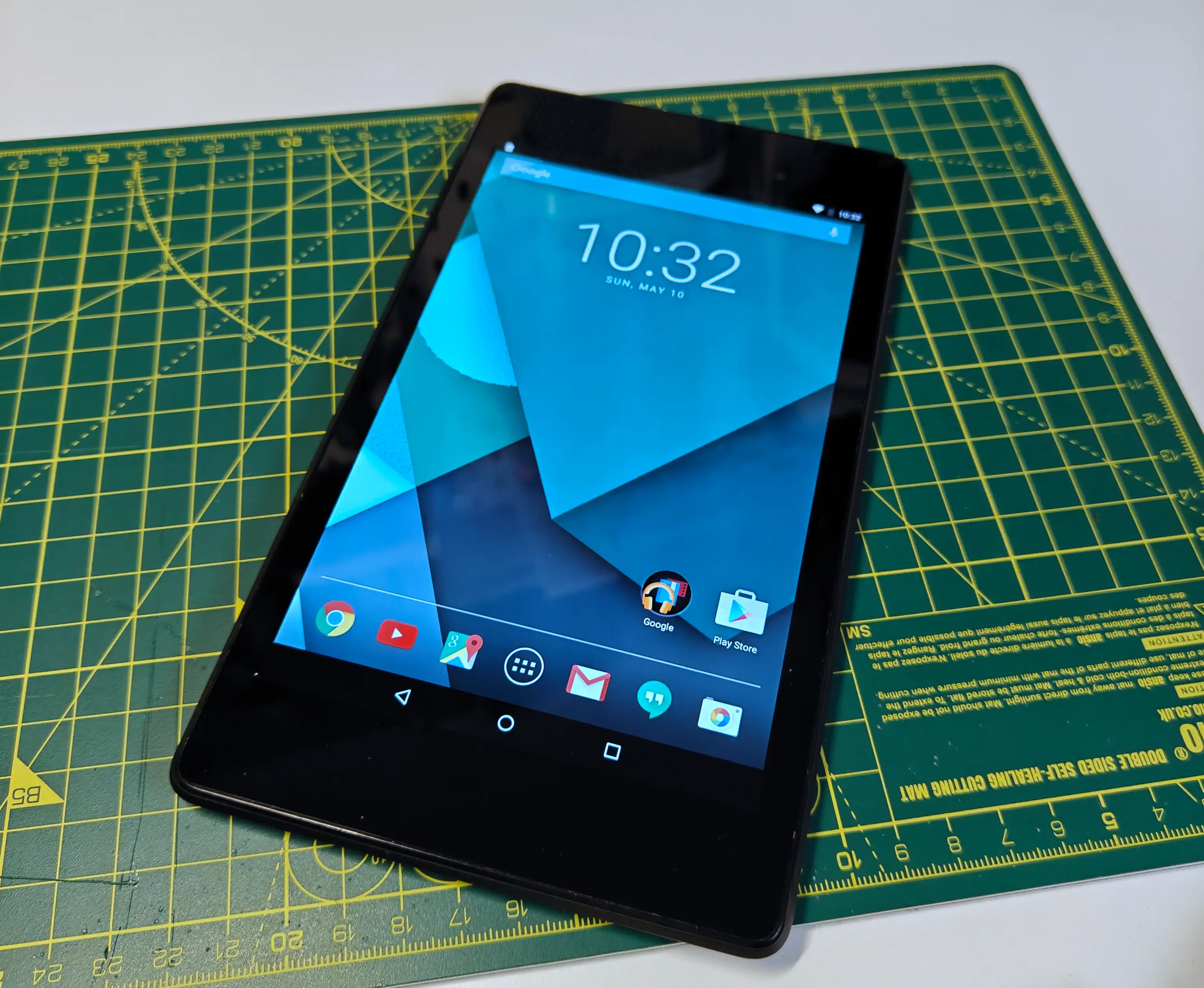 A Nexus 7 tablet, screen up, showing a clock and a blue layered background. The user and icons reflect an older version of Android.