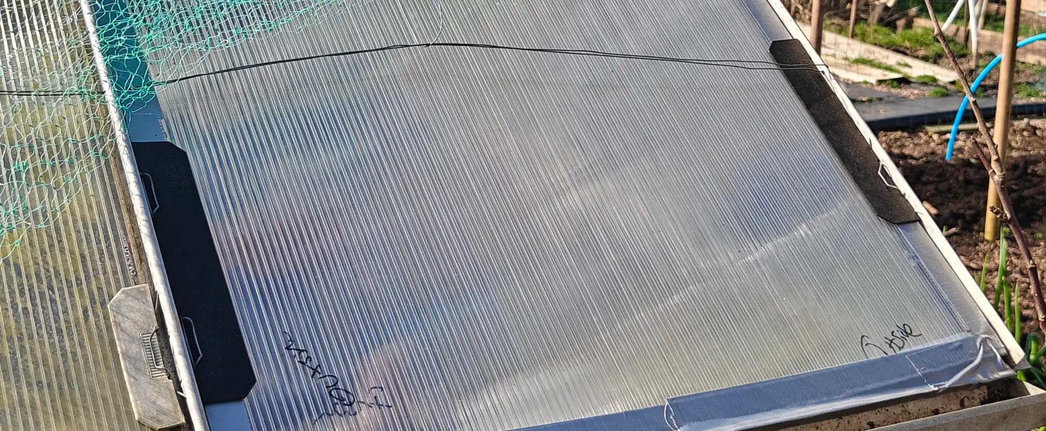 A greenhouse panel, with two black strips on either side, with metal clips on top