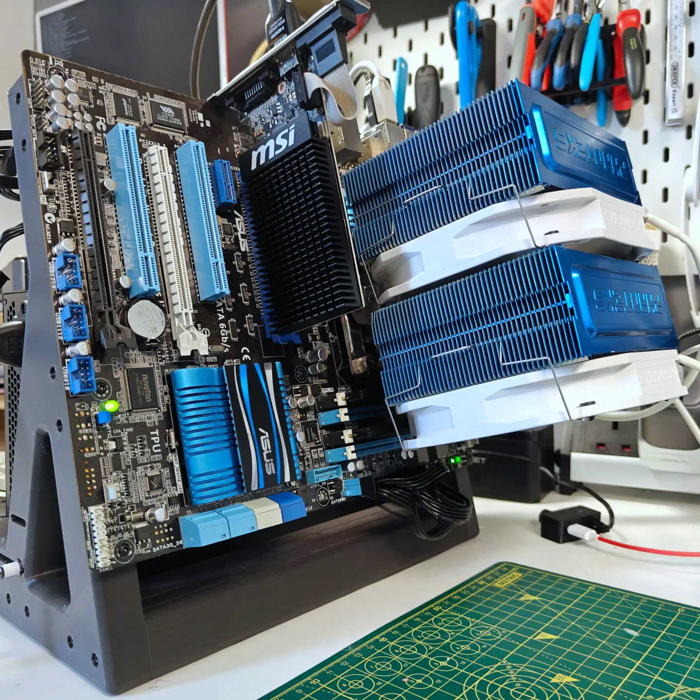 A vertically standing PC motherboard. The board is black, with blue and white highlights. It had a large blue CPU cooler attached which itself has two white fans